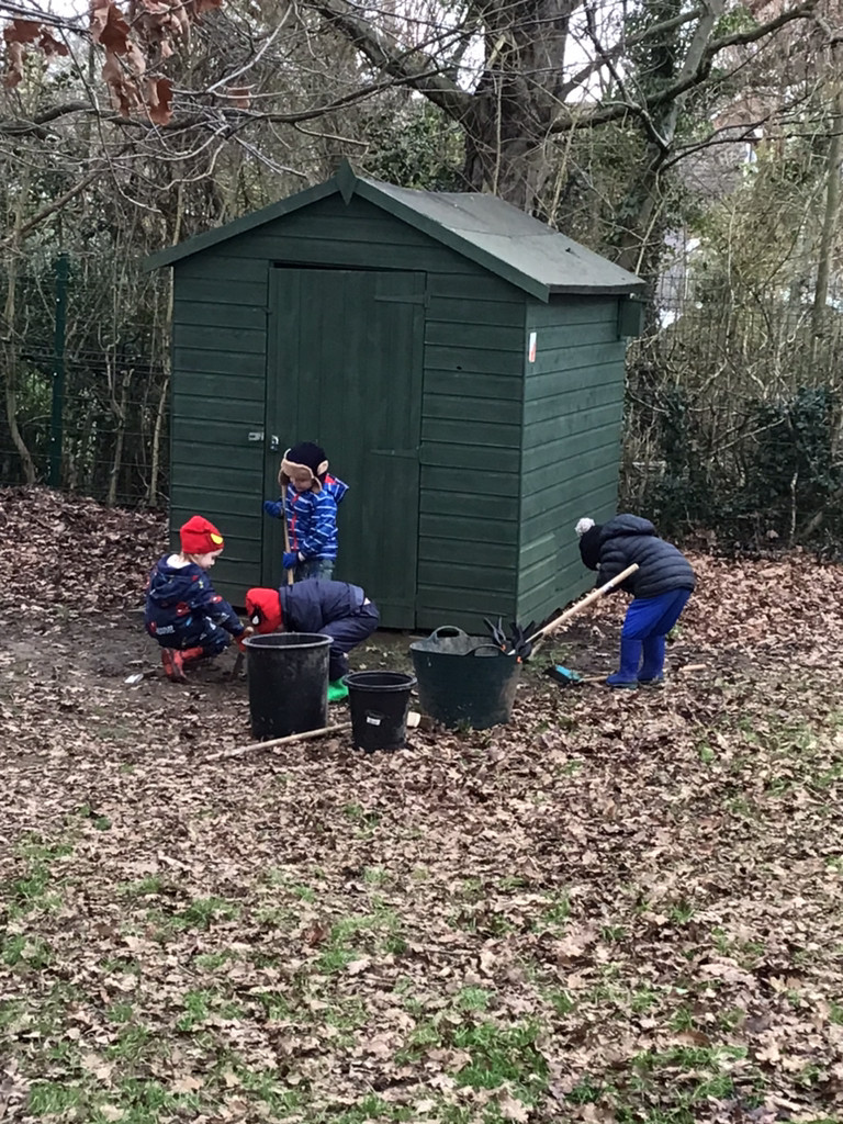 Children raking leaves by shed in forest school area 